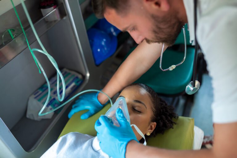 paramedic healthcare emergency staff taking care of a lying down young woman patient on stretcher with medical ventilator system and bag-valve masks inside an medical service ambulance car.